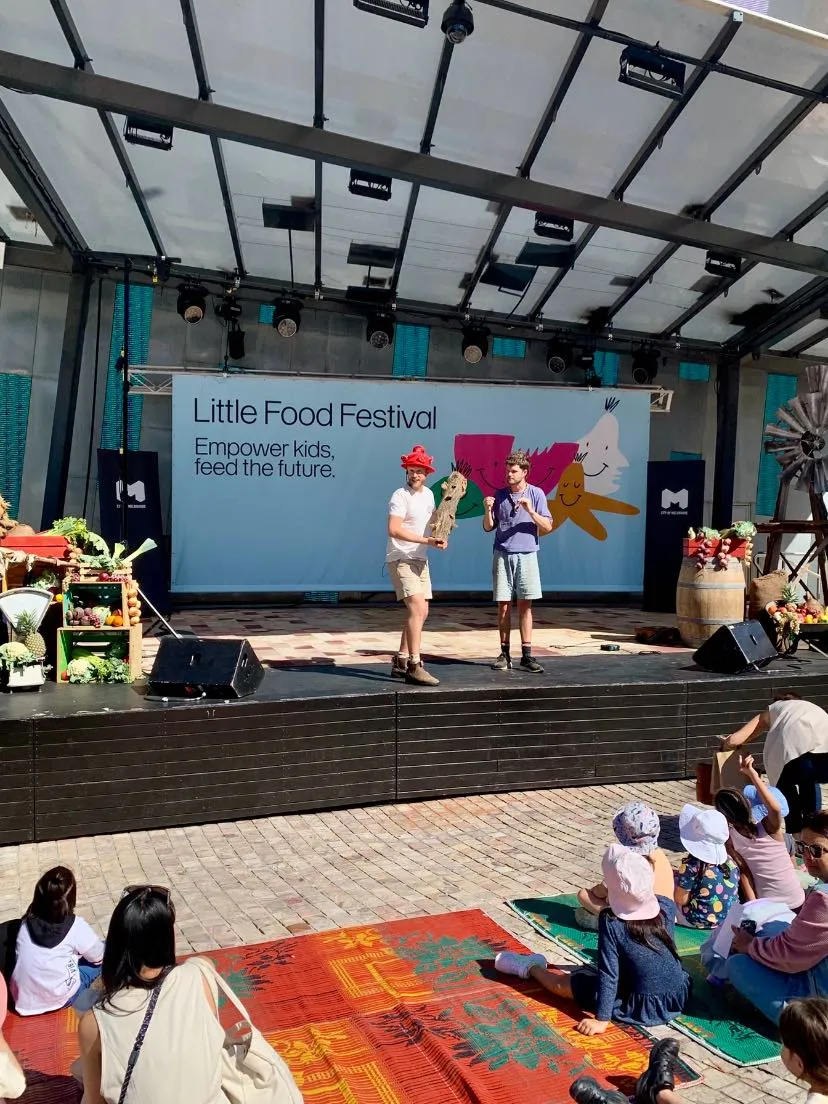 Tom Allen on stage at the Little Food Festival with a young participant and an audience of children