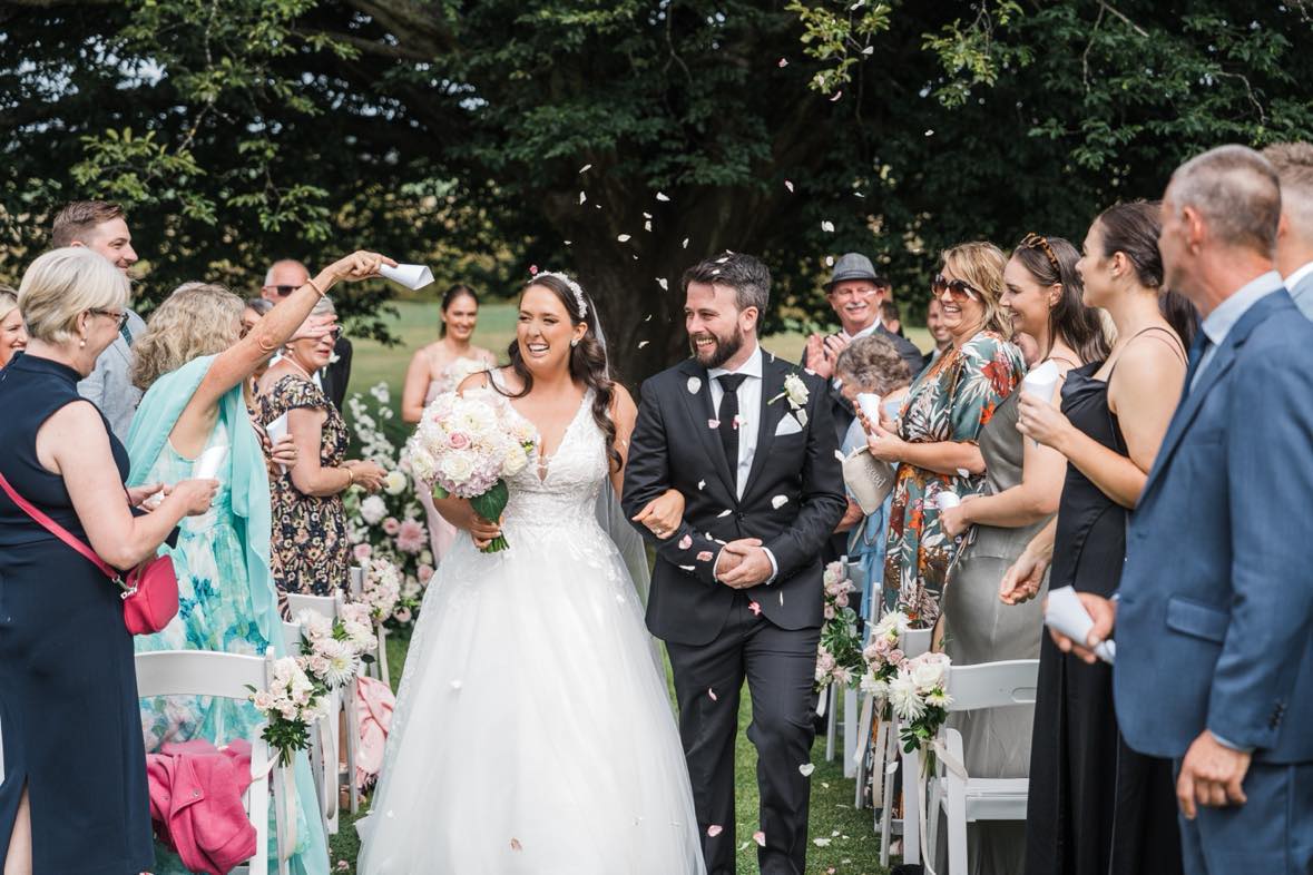 Newlyweds walking back up the aisle as guests shower them with confetti at an outdoor garden wedding