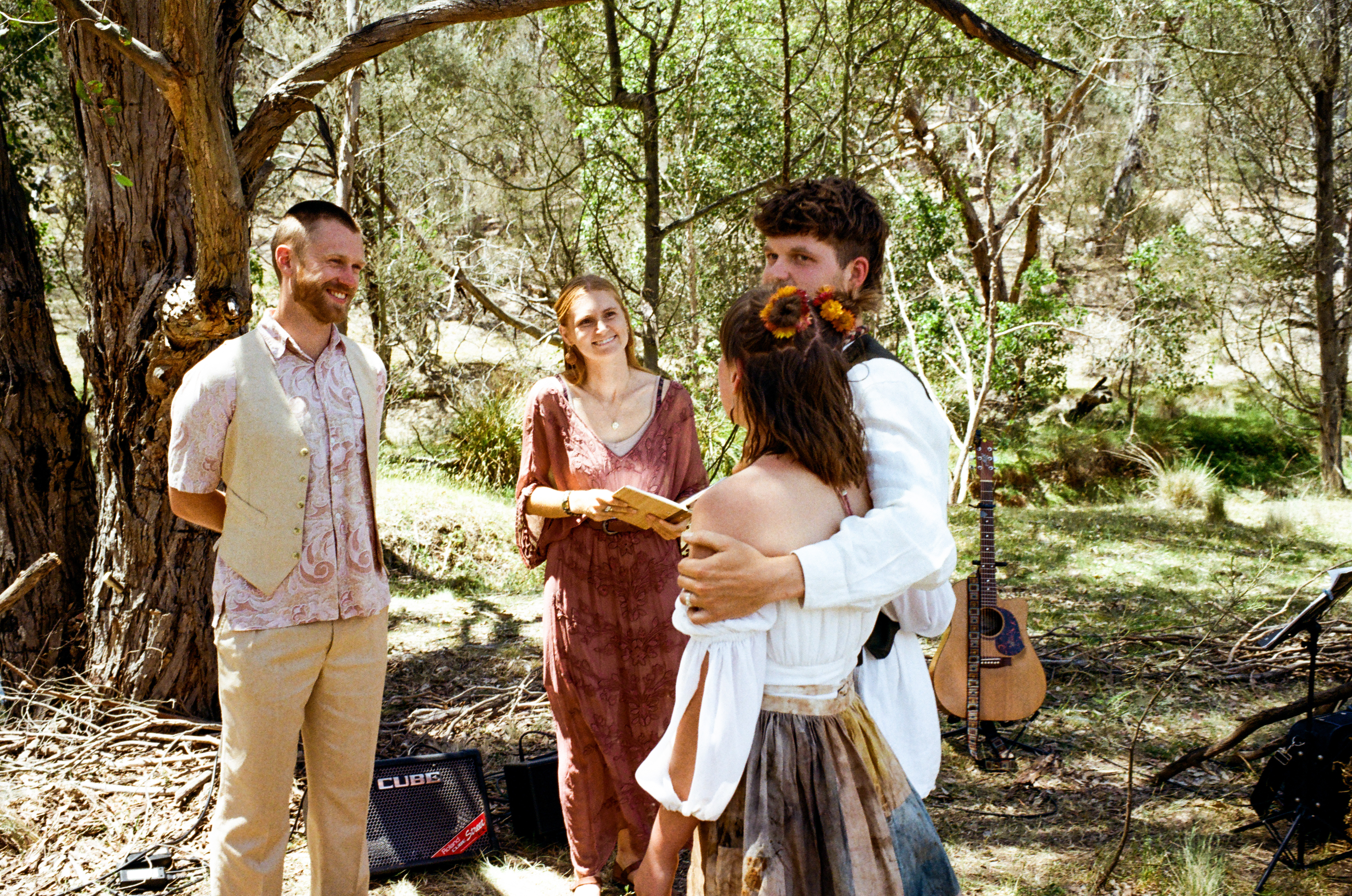 Tom Allen watching as a newly married couple embrace at a relaxed bohemian bush wedding ceremony