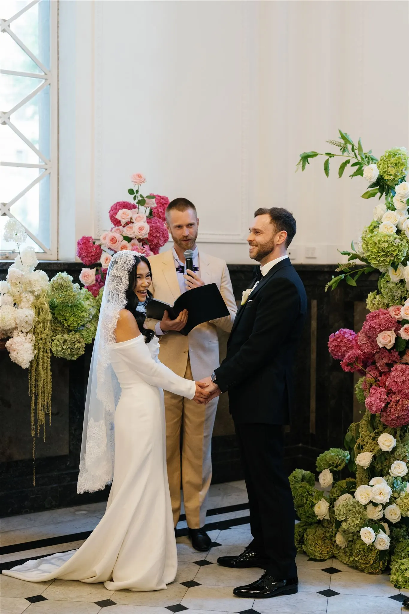 Tom Allen officiating a same-sex wedding ceremony, two grooms holding hands at an intimate indoor venue