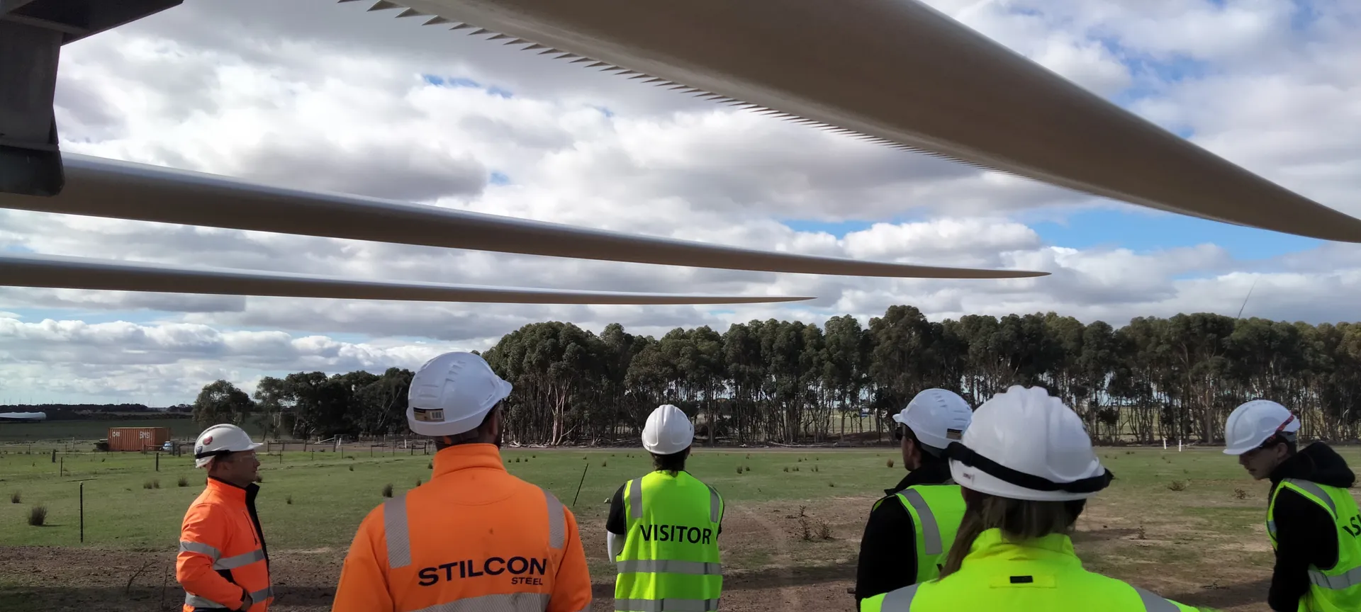 Program participants standing under wind turbine blades on an industry site visit